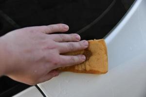 lavar un auto blanco con una esponja a mano foto