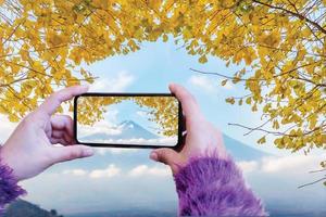 Woman hand take a photo mount fuji with ginkgo leaves by smartphone