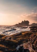 Pura Tanah Lot temple on clifftop and wave hitting on sunset beach in Bali photo