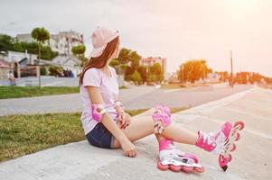 Portrait of a gorgeous young woman in casual clothes and cap sitting on the ground next to the lake. photo