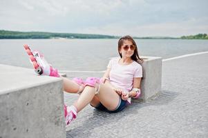 Portrait of a beautiful woman sitting on the ground next to concrete cube wearing rollerblades and casual clothes. photo