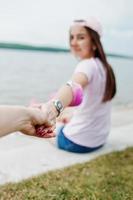 Close-up photo of couple holding hands while sitting on the ground next to the lake.