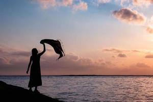 Asian woman relaxing with raised up the cloth on tropical sea with colorful sky photo