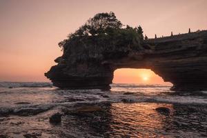 Sunset through of rocky cliff on seashore at sunset. Pura Batu Bolong, Bali