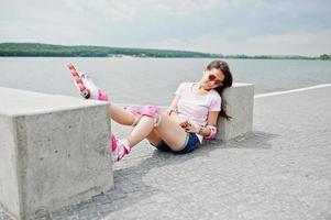 Portrait of a beautiful woman sitting on the ground next to concrete cube wearing rollerblades and casual clothes. photo