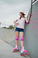 Good-looking young woman wearing cap, t-shirt and shorts pose in rollerblades on the skatepark. photo