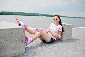 Portrait of a beautiful woman sitting on the ground next to concrete cube wearing rollerblades and casual clothes. photo