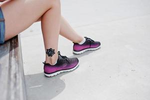 Close-up photo of female tattooed legs in purple sneakers.