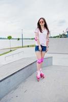 retrato de una mujer joven hermosa en pantalones cortos, camiseta y gafas de sol de pie al aire libre en patines. foto