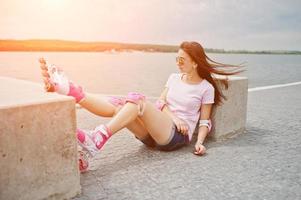 Portrait of a beautiful woman sitting on the ground next to concrete cube wearing rollerblades and casual clothes. photo