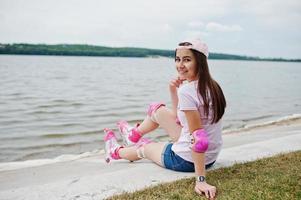 retrato de una joven hermosa con ropa informal y gorra sentada en el suelo junto al lago. foto