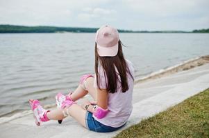 Portrait of a gorgeous young woman in casual clothes and cap sitting on the ground next to the lake. photo