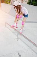 retrato de una hermosa chica con gorra, camiseta y pantalones cortos poniéndose patines al aire libre junto al lago. foto