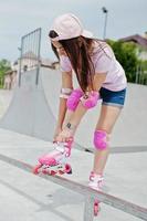Portrait of a beautiful girl wearing cap, t-shirt and shorts putting on rollerblades outdoor next to the lake. photo