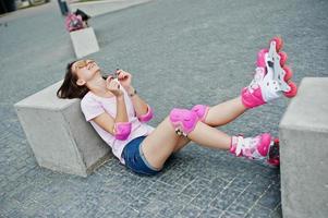 Portrait of a beautiful woman sitting on the ground next to concrete cube wearing rollerblades and casual clothes. photo