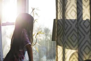 Little girl looking out a window on a sunny day photo