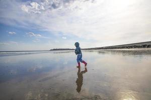 niña con botas rosas caminando en una playa foto
