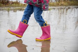 niña con botas rosas caminando por un camino fangoso foto