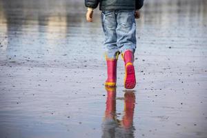 Little girl with pink boots walking on a beach photo