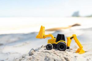 juguete retroexcavadora de plástico amarillo en la arena de la playa foto