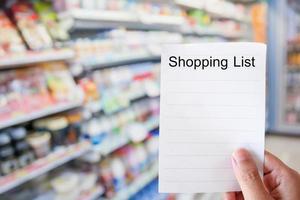 hand holding shopping list paper with convenience store shelves photo
