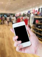 mano de mujer sostenga el teléfono inteligente, tableta, teléfono celular en el fondo de la tienda de ropa borrosa foto