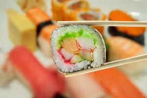 Sushi in chopsticks with blur sushi on a plate background photo