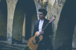 boy holds guitar leaning against a wall in vintage style photo