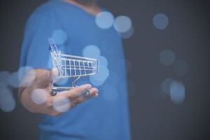 A man holding a toy shopping cart empty on hand with copy space for text or design, background. sale, discount, shopping online concept. Consumer society trend. photo