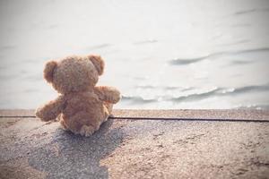 un oso de peluche triste se sienta solo en un puente mirando el mar en soledad con espacio para copiar. juguete, muñeca, para niño.