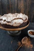round baked brownie cake topped with meringue and chocolate swirls on rustic cake stand