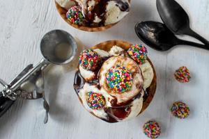 vanilla ice cream scoops with colorful candy pieces and chocolate syrup in waffle cone bowl on rustic white background photo