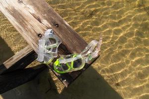 sun washed bench with diving goggles over bay water in sunlight photo