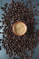 copper cup filled with espresso coffee in center of raw coffee beans spread out on rustic table flat lay photo