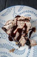 slice of baked brownie dessert topped with meringue and chocolate swirls and drizzled chocolate syrup photo