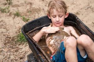 young boy playing in mud in wheelbarrow filled with water