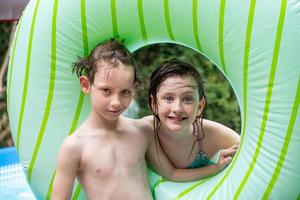 una niña y un niño sonrientes y felices mirando a través del flotador redondo de la piscina en la soleada piscina del patio trasero foto