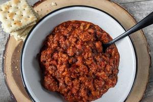 warm bowl of chili and beans with crackers in rustic setting flat lay