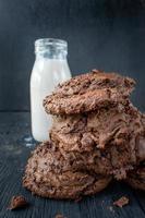 stack of chocolate chip cookies with milk on rustic wood table photo