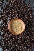 copper cup filled with espresso coffee in center of raw coffee beans spread out on rustic table flat lay photo