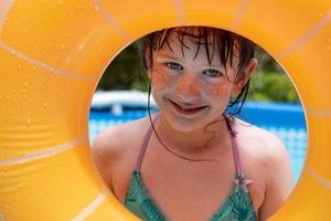 una joven sonriente y feliz mirando a través de un flotador redondo en la soleada piscina del patio trasero foto