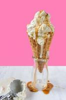 melting vanilla ice cream scoops with dripping caramel sauce over waffle cone on fun vibrant pink background