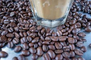 glass of creamy coffee in center of raw coffee beans spread out on rustic table photo