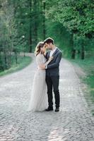 couple in wedding attire with a bouquet of flowers and greenery is in the hands against the backdrop of the field at sunset, the bride and groom photo