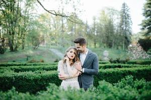 pareja vestida de boda con un ramo de flores y vegetación está en las manos contra el telón de fondo del campo al atardecer, la novia y el novio foto