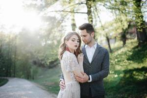 pareja vestida de boda con un ramo de flores y vegetación está en las manos contra el telón de fondo del campo al atardecer, la novia y el novio foto