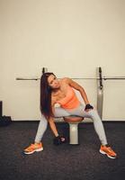 attractive girl raises dumbbell sitting in the gym photo