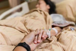 mano del marido sosteniendo la mano de su esposa en la cama en la habitación del hospital. foto