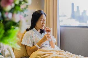 mujer paciente bebiendo agua mientras está sentada en la cama en el hospital.