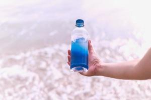 Woman holding bottle mineral water in her hand on the beach.
